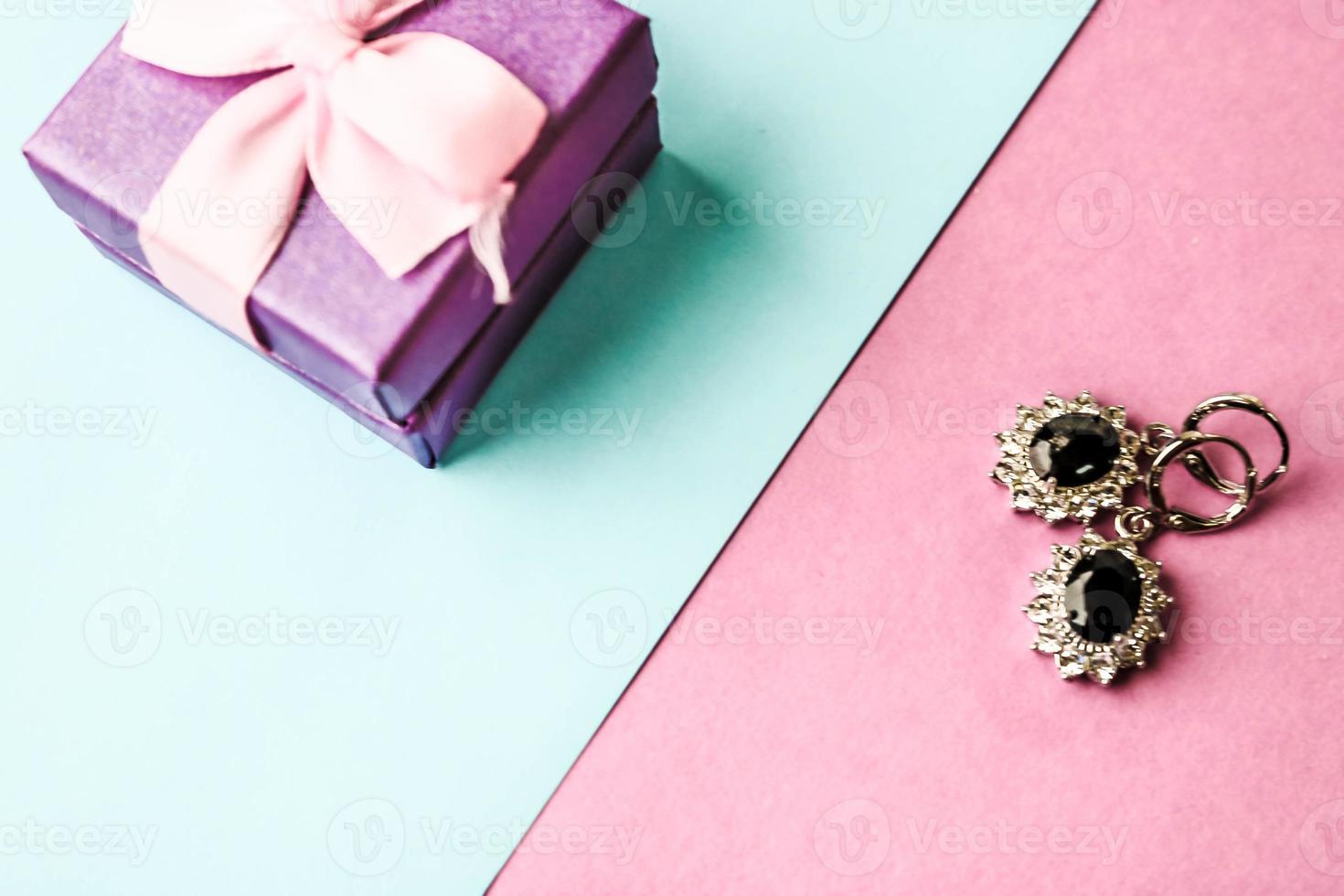 caixa de beleza, caixa de presente linda festiva com um laço com brincos de prata com pedras preciosas em um fundo rosa roxo e azul. postura plana. vista do topo foto