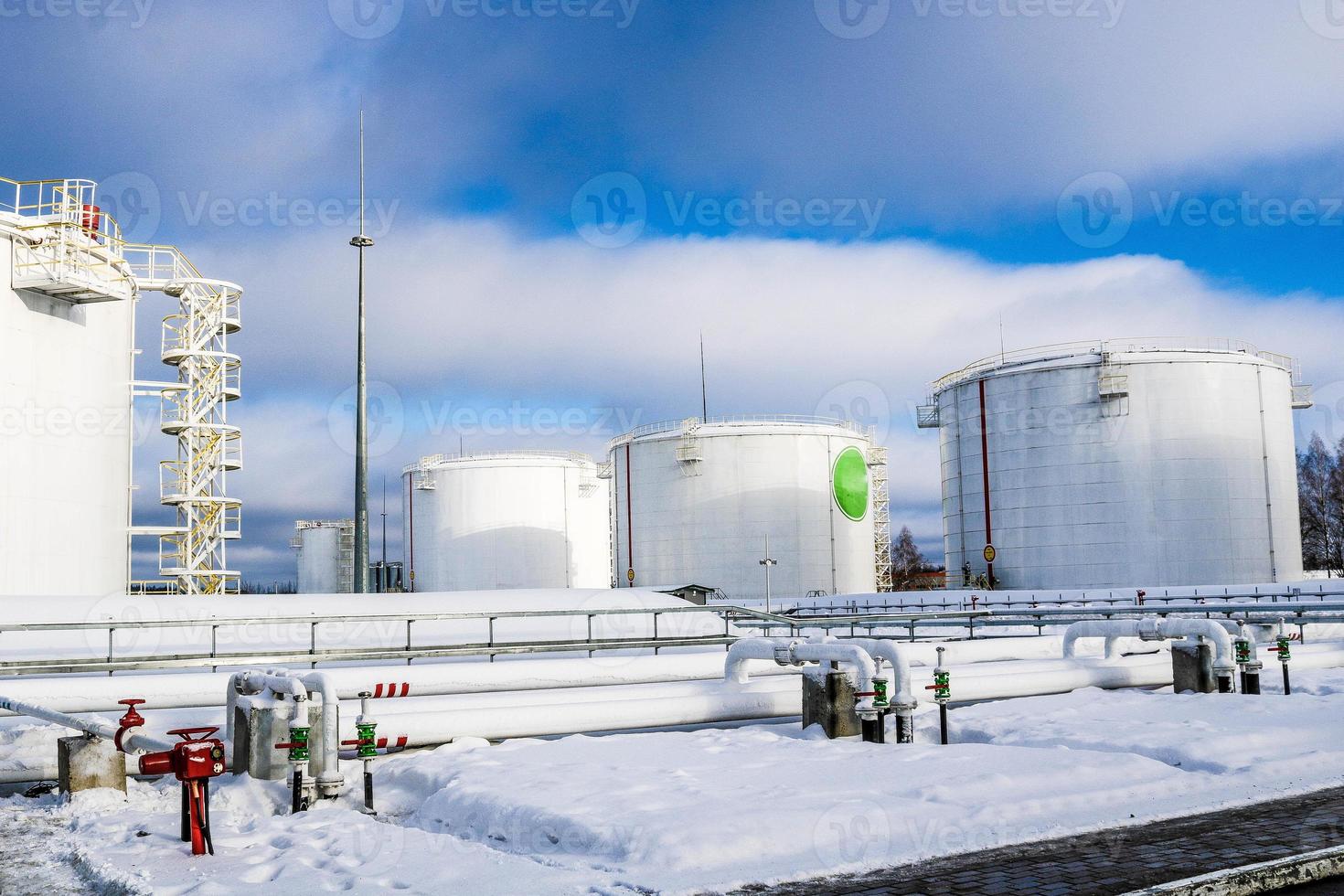 grandes tanques industriais de metal de ferro branco para armazenamento de combustível, gasolina e diesel e encanamento com válvulas e flanges na refinaria no inverno foto
