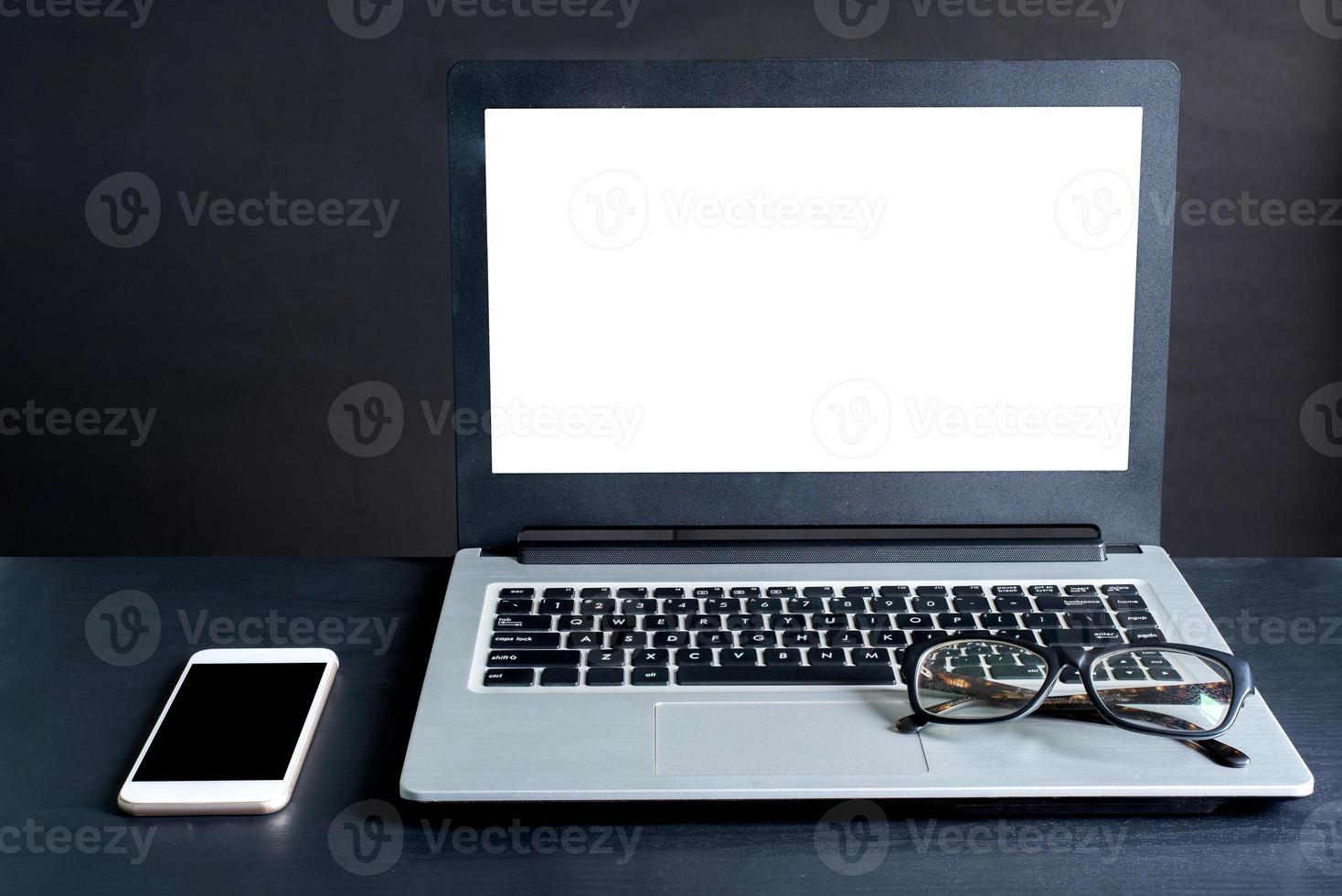 laptop, smartphone, óculos, na mesa de madeira preta com fundo preto foto
