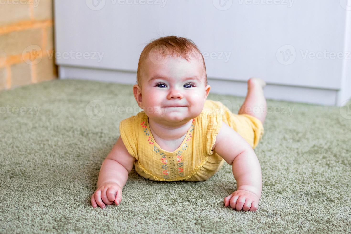 retrato de sorridente menina caucasiana de vestido amarelo. criança tentando engatinhar no chão. foto