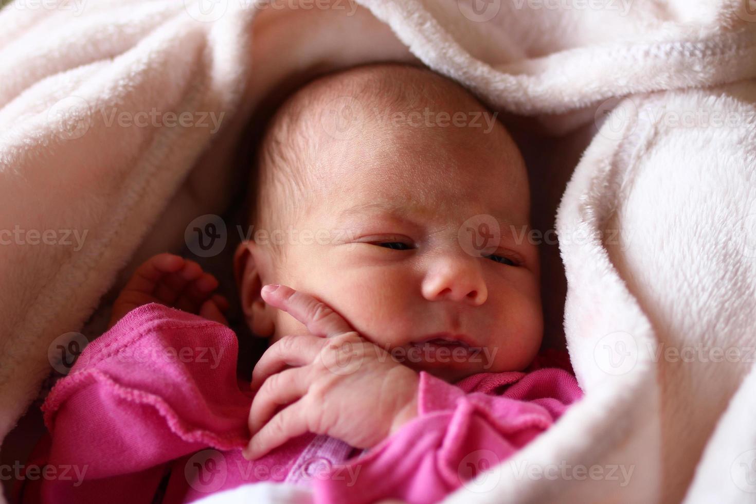 lindo bebê recém-nascido dormindo em rosa baud na cama dela sob o cobertor bege. foto