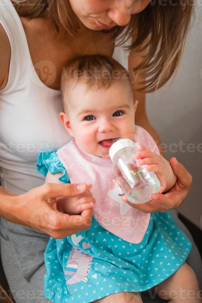 mãe ajuda a filha a beber água. criança aprende a segurar uma garrafa. foto