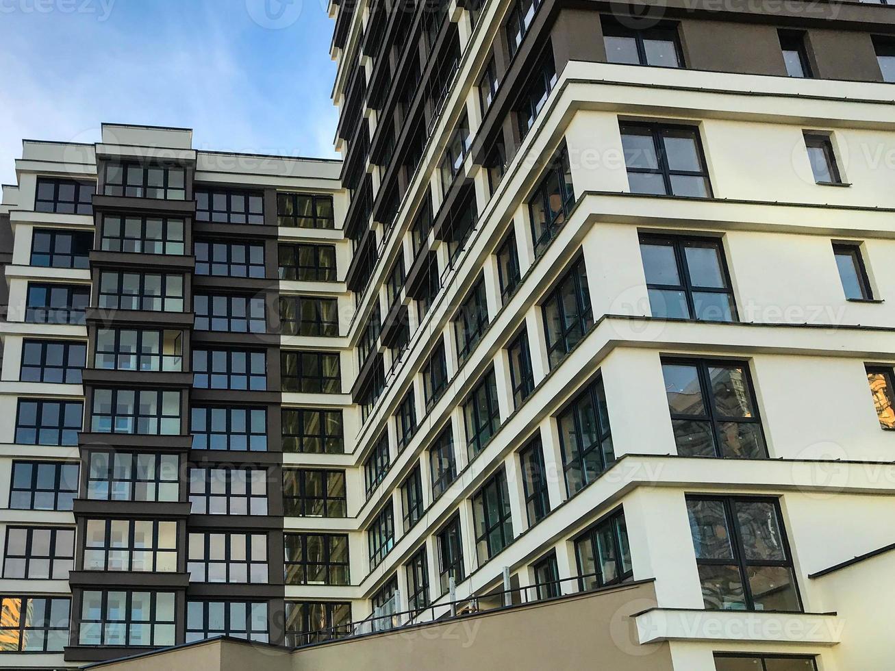 um edifício de vários andares com muitas janelas fica na cidade. decoração marrom e branca. molduras pretas nas janelas, vidros panorâmicos. design elegante, paisagem urbana foto