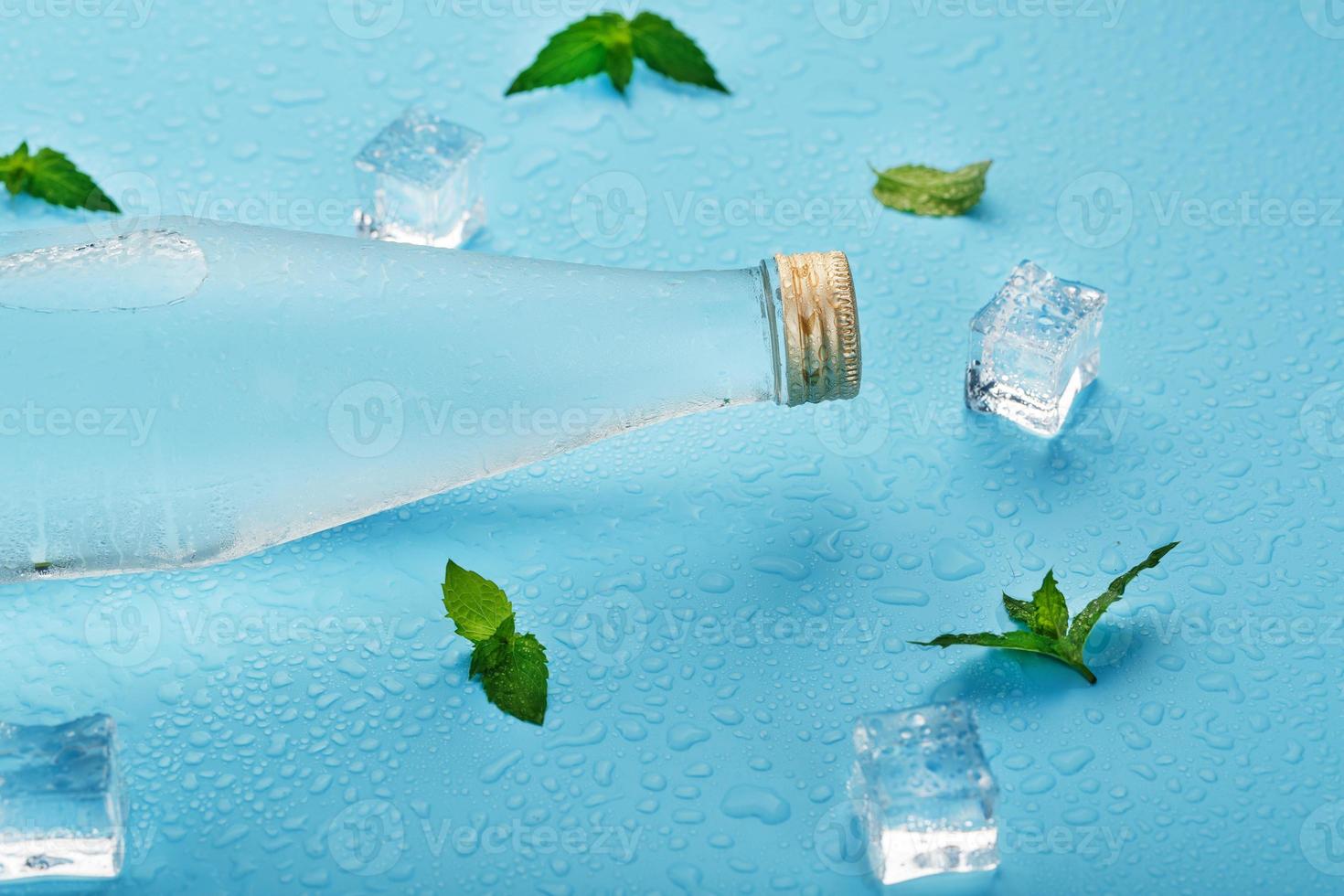 garrafa com uma bebida gelada, cubos de gelo, gotas e folhas de hortelã em um fundo azul. foto