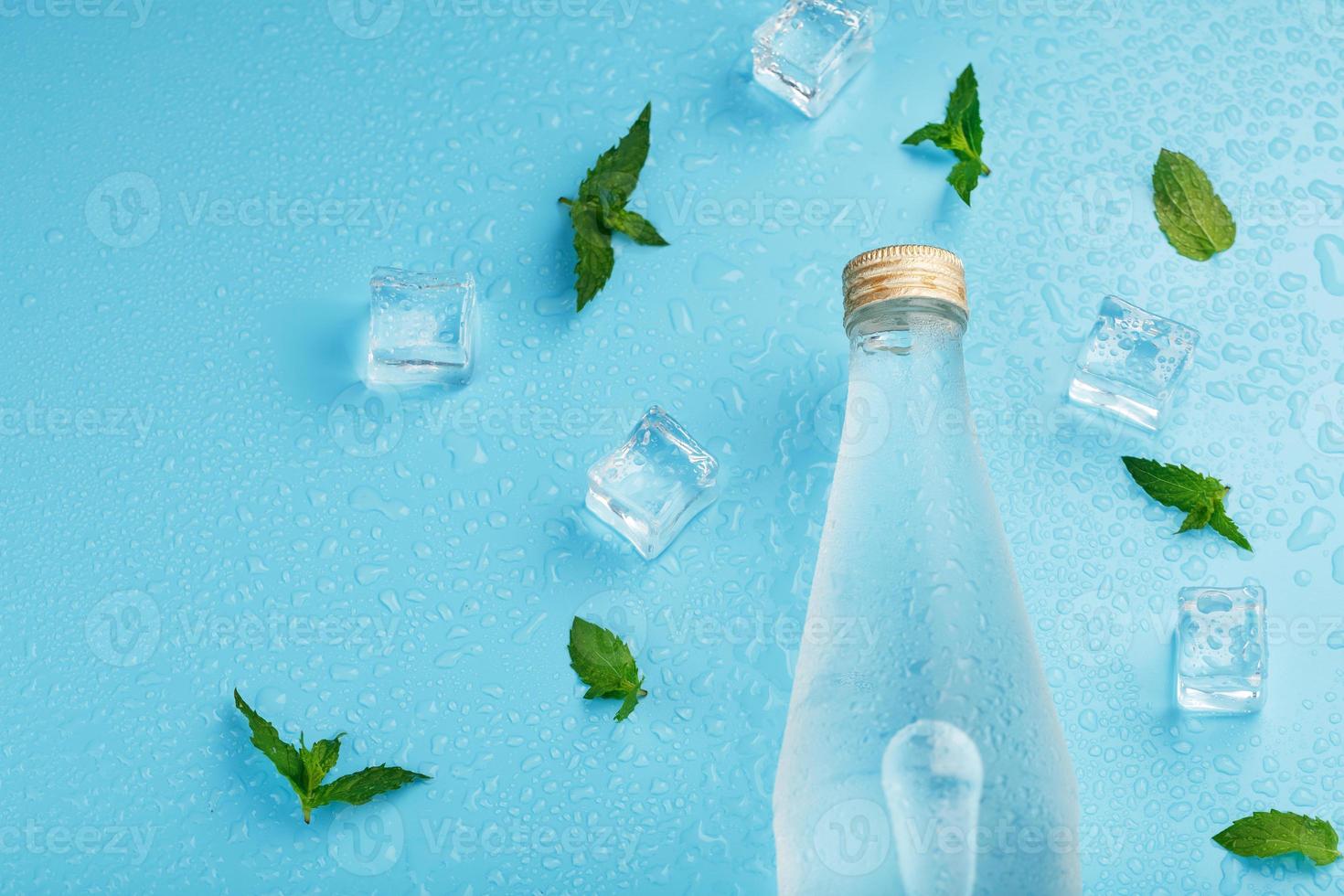 garrafa com uma bebida gelada, cubos de gelo, gotas e folhas de hortelã em um fundo azul. foto