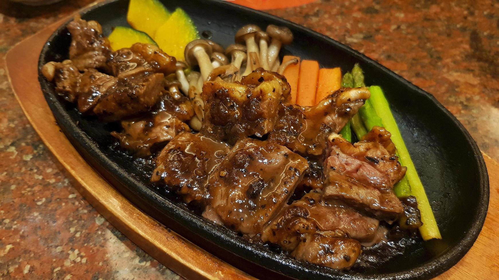 bife de áustria com cenoura fatiada, abóbora, cogumelos e aspargos na panela preta quente no restaurante. deliciosa carne com molho de molho e pimenta na cobertura. foto