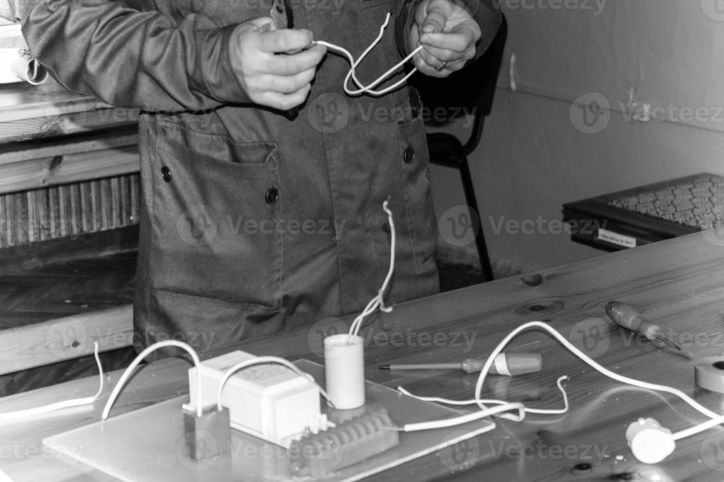 um homem que trabalha eletricista trabalha, coleta o circuito elétrico de uma grande lâmpada de rua branca com fios, um relé em uma fábrica de planta industrial foto