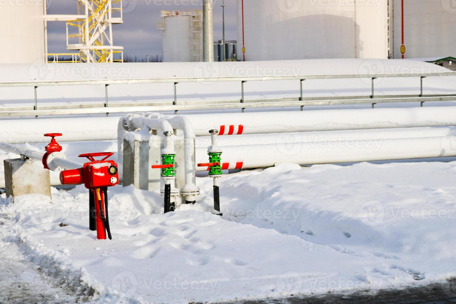 grandes tanques industriais de metal de ferro branco para armazenamento de combustível, gasolina e diesel e encanamento com válvulas e flanges na refinaria no inverno foto