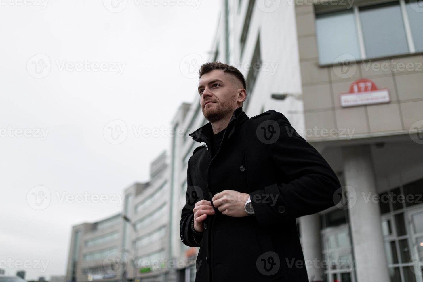 elegante jovem brutal no fundo de um edifício da cidade com um casaco preto foto