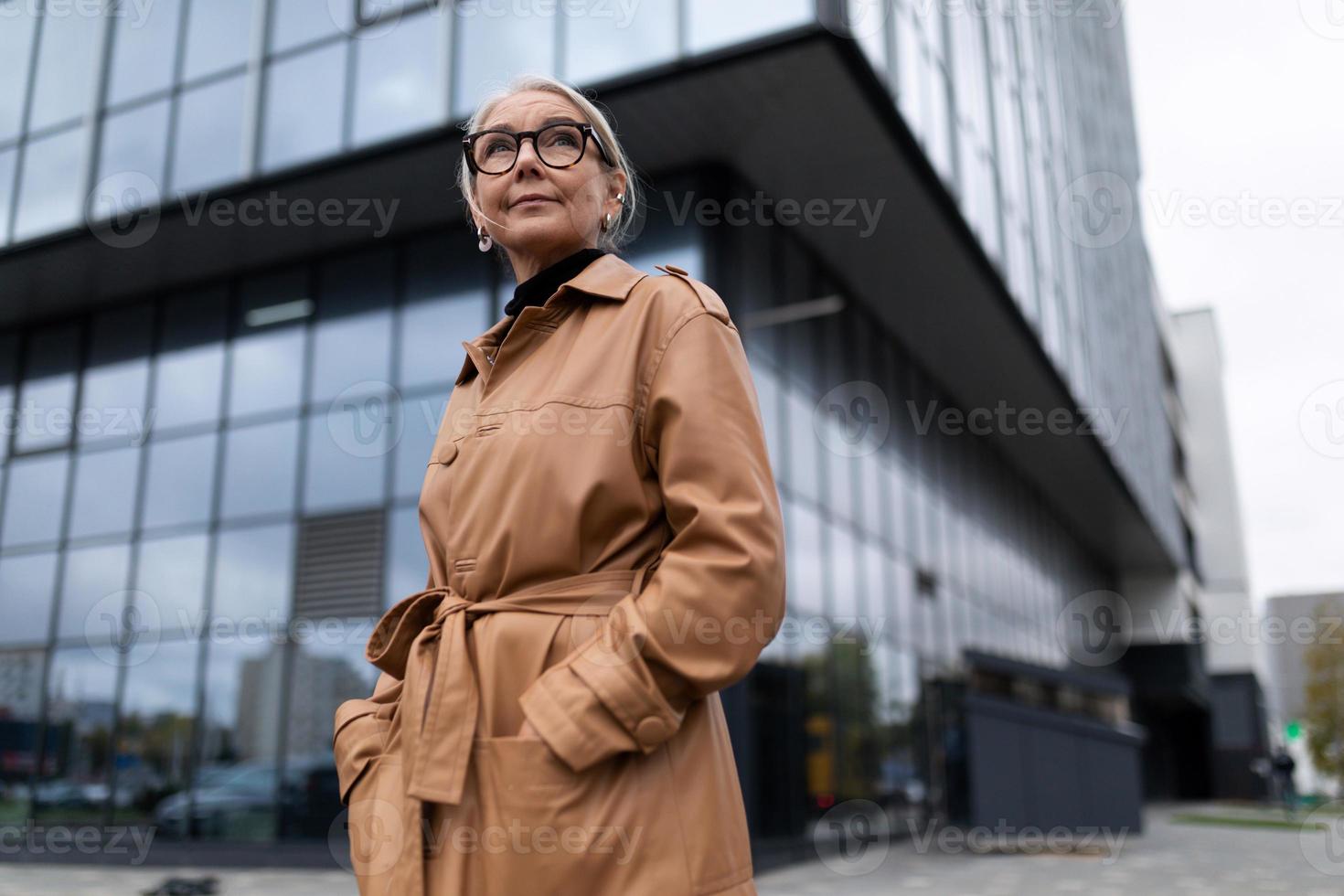 cabeça de mulher idosa bem sucedida no fundo da fachada de um prédio de escritórios moderno foto