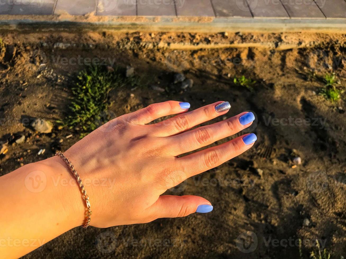 mão com manicure azul sobre fundo de areia. uma nova cor de unhas para uma menina com uma pulseira de ouro. ao fundo - a construção de uma nova área, sujeira e materiais de construção. foto