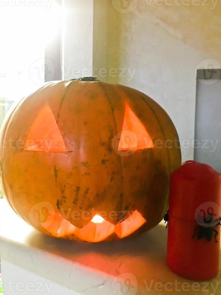 grande abóbora redonda assustadora luminosa amarela alaranjada terrível com olhos triangulares esculpidos e uma boca para o feriado de halloween e uma vela vermelha com aranhas foto