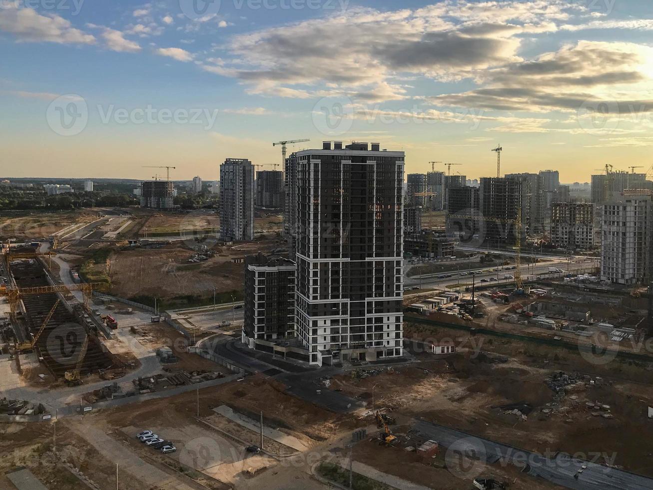 um novo bairro da cidade. atirando de uma altura. paisagem urbana urbana. uma casa alta de vidro marrom se ergue contra o pano de fundo da área em construção. perto de guindastes de construção altos foto