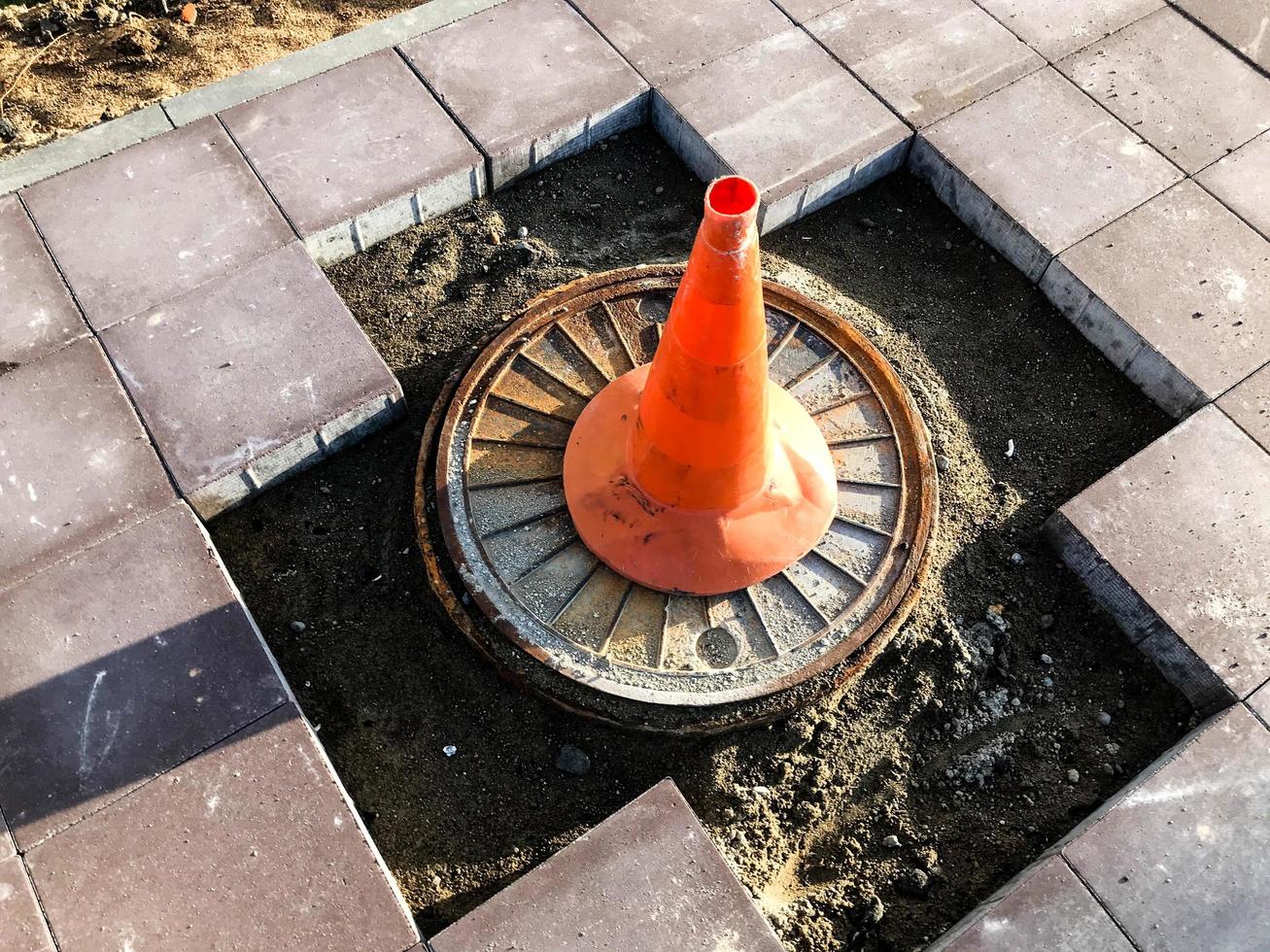 um cone laranja fica em uma seção perigosa da estrada. a marca de identificação em uma cor clara e distinta fica em um buraco na estrada. a superfície da estrada é deslocada foto