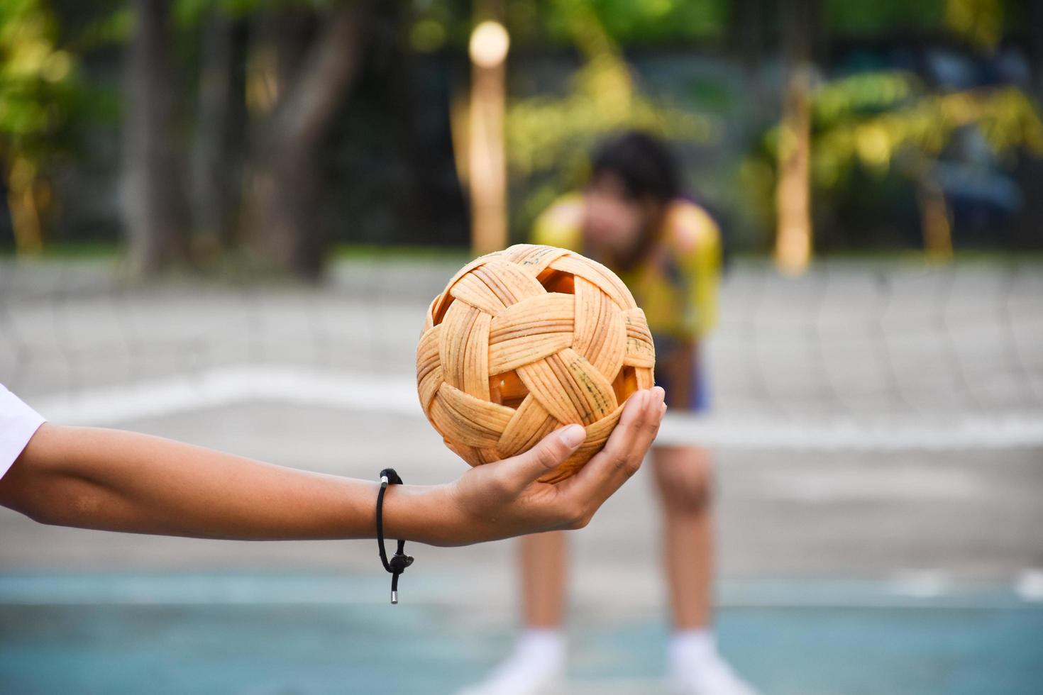 bola sepak takraw, esporte tradicional dos países do sudeste asiático, segurando na mão do jovem jogador sepak takraw feminino asiático na frente da rede antes de jogá-lo para outro jogador para chutar a rede. foto