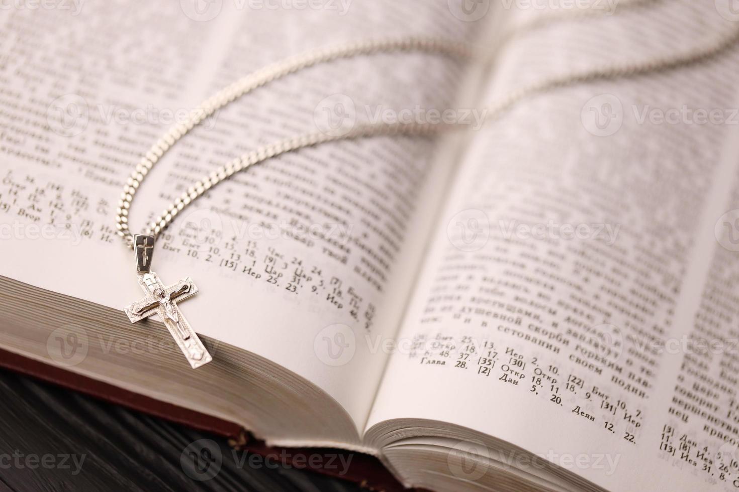 colar de prata com cruz crucifixo no livro da bíblia sagrada cristão na mesa de madeira preta. pedindo bênçãos de deus com o poder da santidade, que traz sorte foto