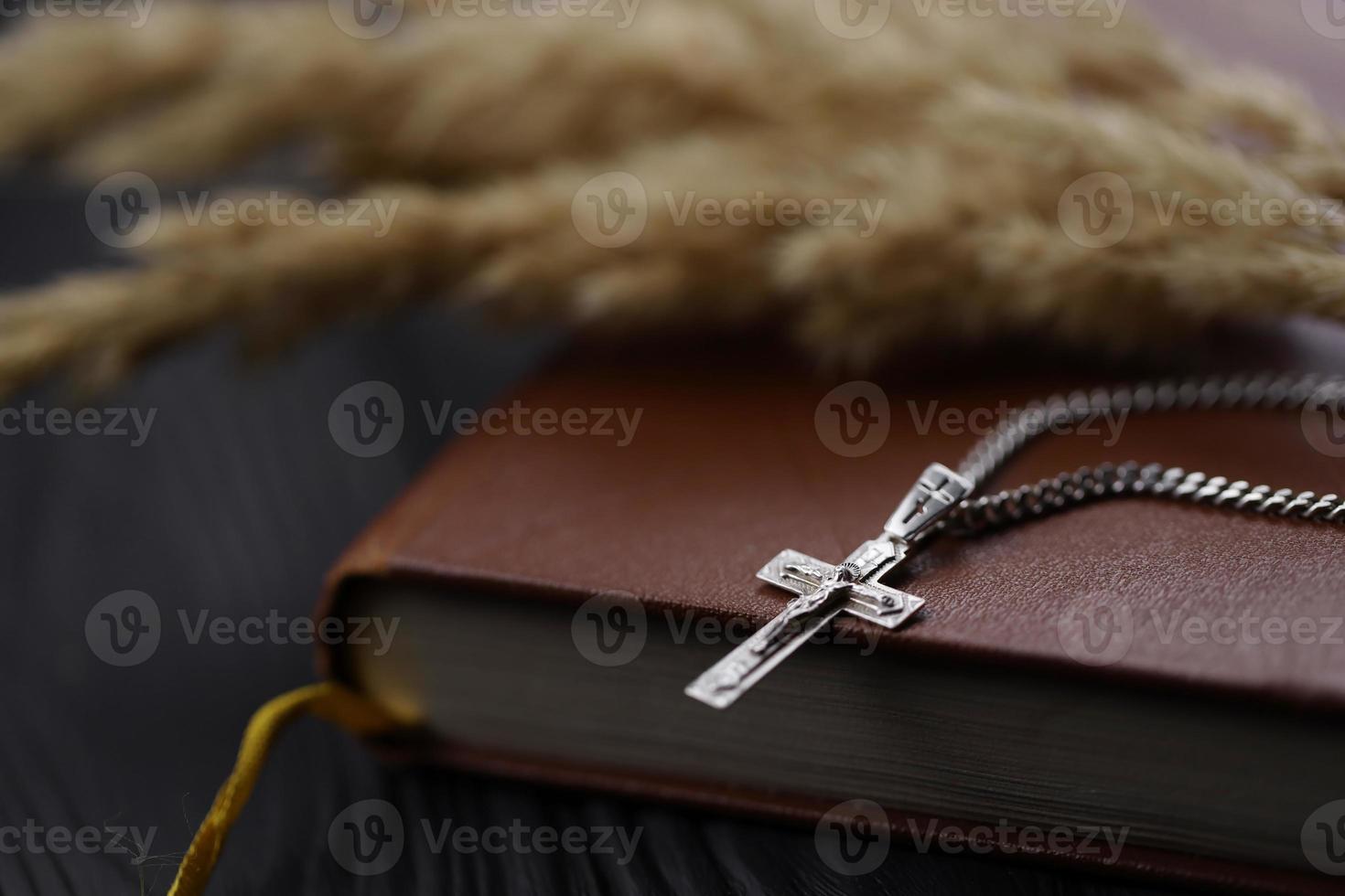colar de prata com cruz crucifixo no livro da bíblia sagrada cristão na mesa de madeira preta. pedindo bênçãos de Deus com o poder da santidade foto
