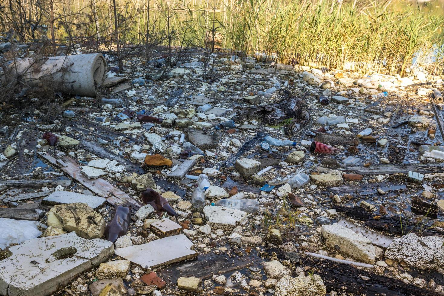 montes de resíduos de construção, lixo doméstico, espuma e garrafas plásticas na margem de um lago florestal, problemas de poluição ambiental foto