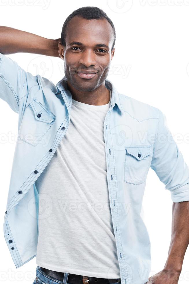 ele sabe que ele é legal. belo jovem negro segurando a mão na cabeça e sorrindo para a câmera em pé contra um fundo branco foto