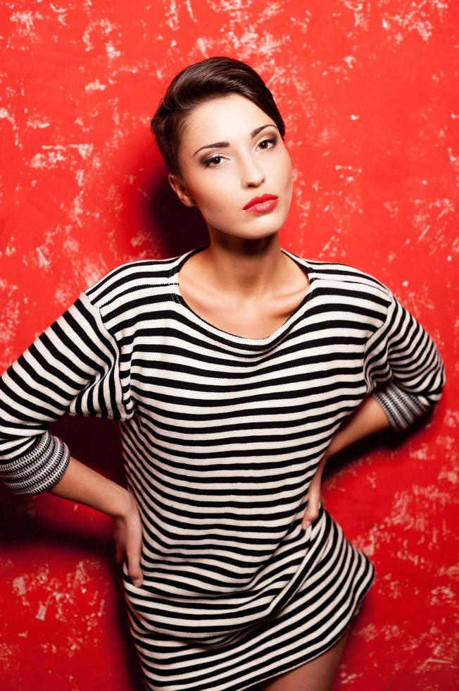 beleza em grande estilo. moda jovem mulher de cabelo curto em roupas listradas posando contra fundo vermelho foto