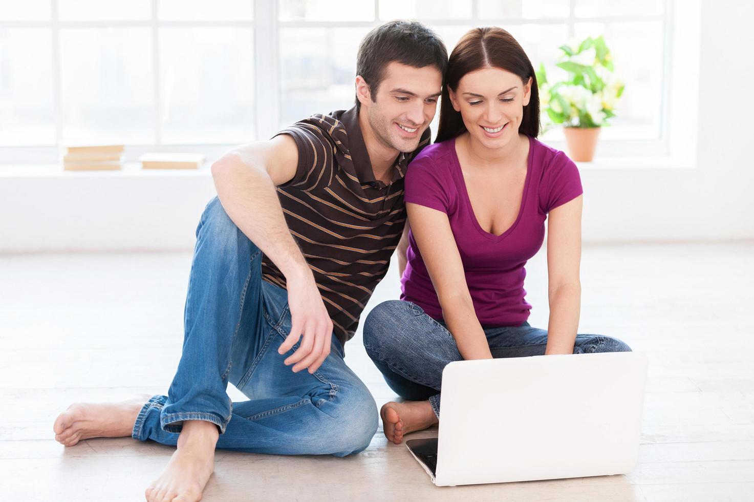 trabalhando em seu laptop. lindo casal jovem trabalhando juntos no laptop enquanto está sentado no chão em seus apartamentos foto