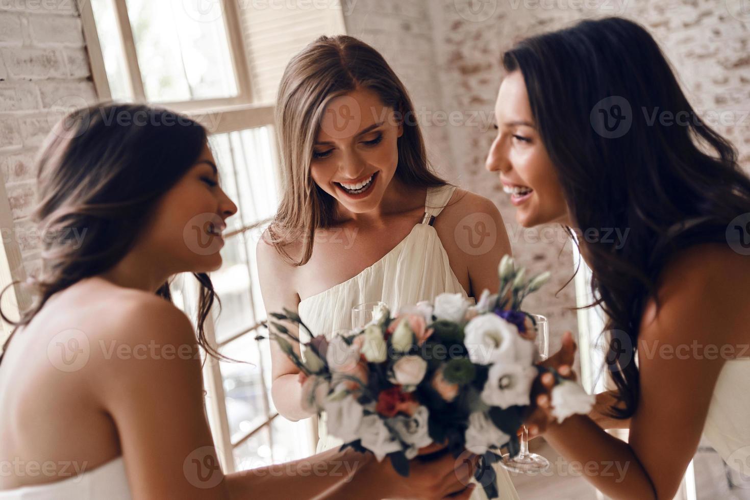 sentindo animado sobre o casamento. atraente jovem noiva segurando um buquê de casamento e sorrindo enquanto conversava com suas encantadoras damas de honra foto