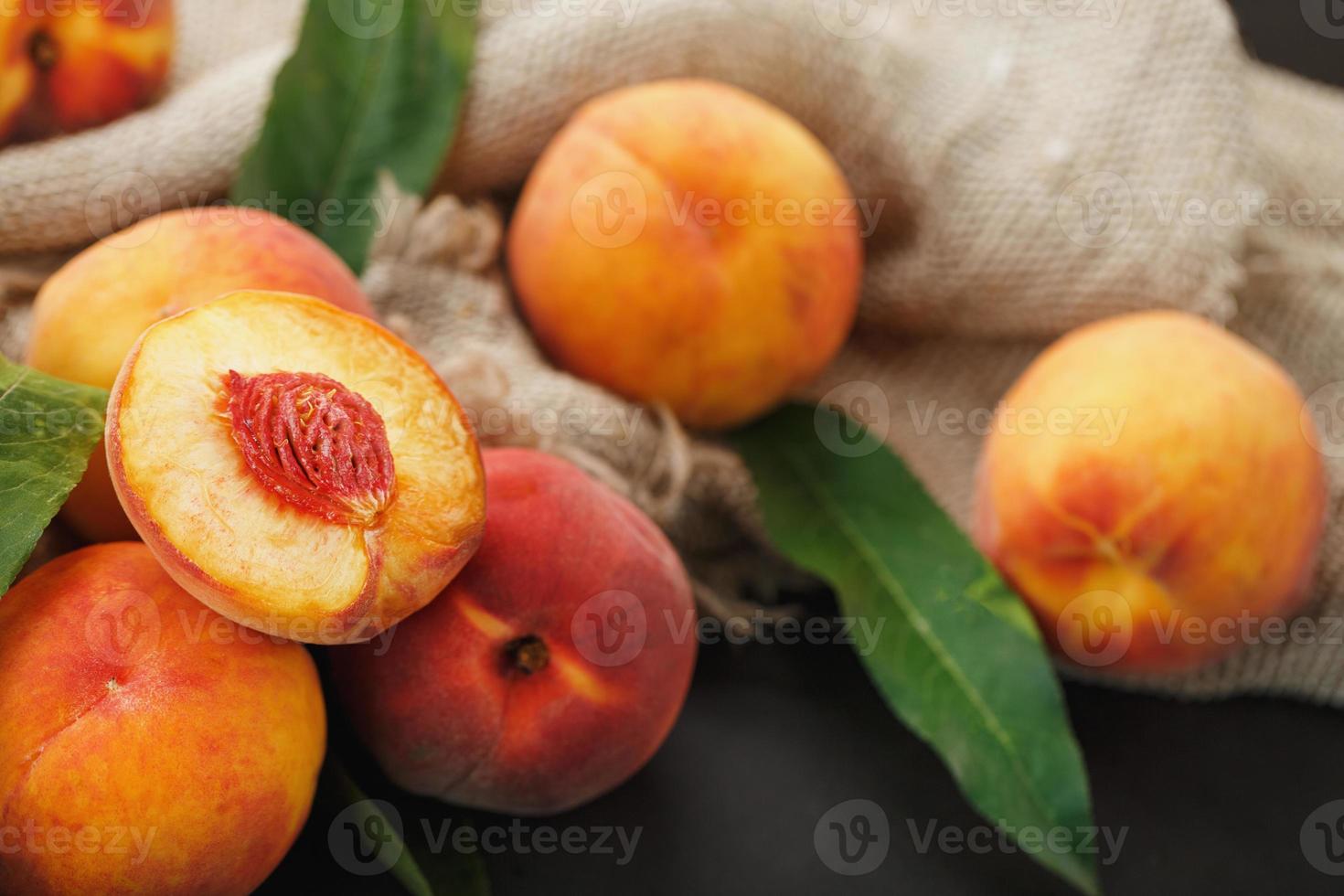 fruta de pêssego em um fundo preto com um pano de serapilheira e folhas verdes. foto