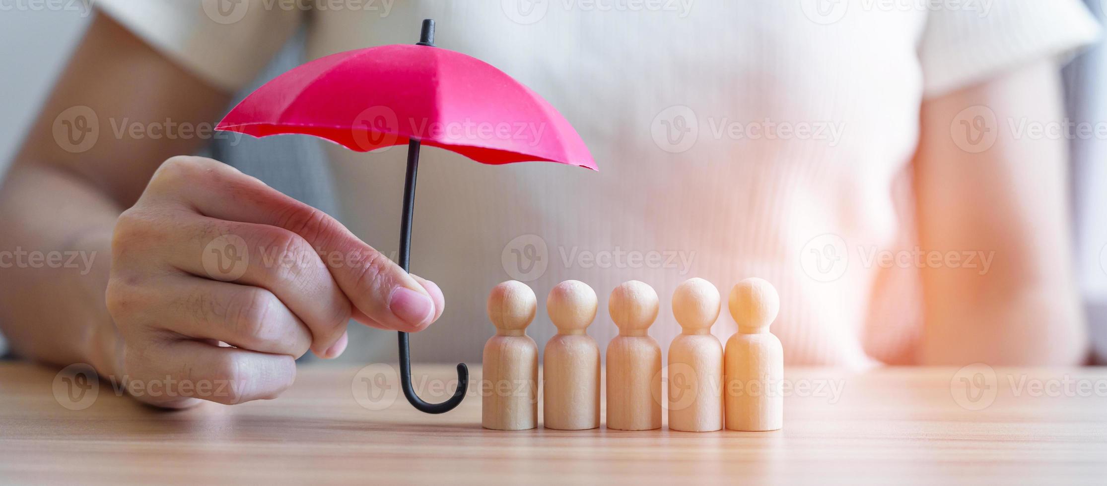 mão segurando o guarda-chuva vermelho e cobrir os homens de madeira da multidão de funcionários. pessoas, negócios, gestão de recursos humanos, seguro de vida, trabalho em equipe e conceitos de liderança foto