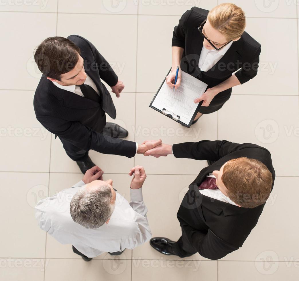 reunião de negócios. vista superior de quatro pessoas em trajes formais em pé perto uma da outra enquanto duas delas apertam as mãos foto