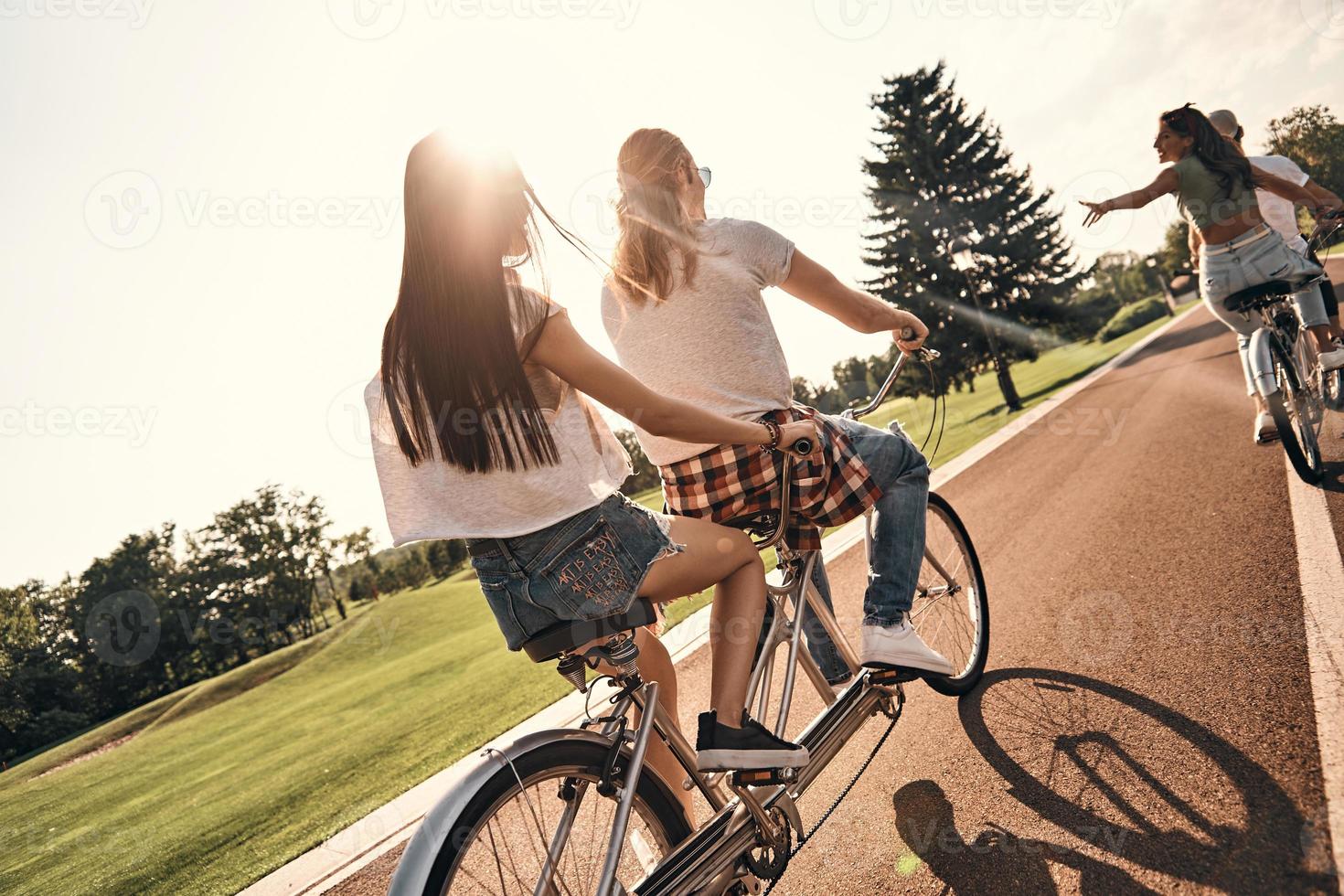 sentindo a estrada. vista traseira de jovens em roupas casuais andando de bicicleta juntos enquanto passam tempo despreocupado ao ar livre foto