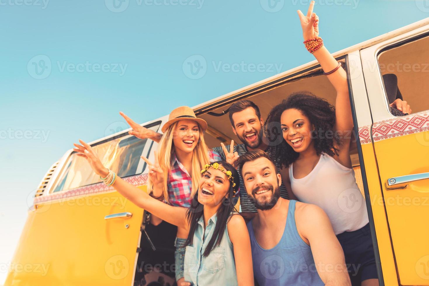 jovem selvagem e livre. vista de ângulo baixo do grupo de jovens felizes se divertindo juntos enquanto está sentado dentro da mini van retrô foto