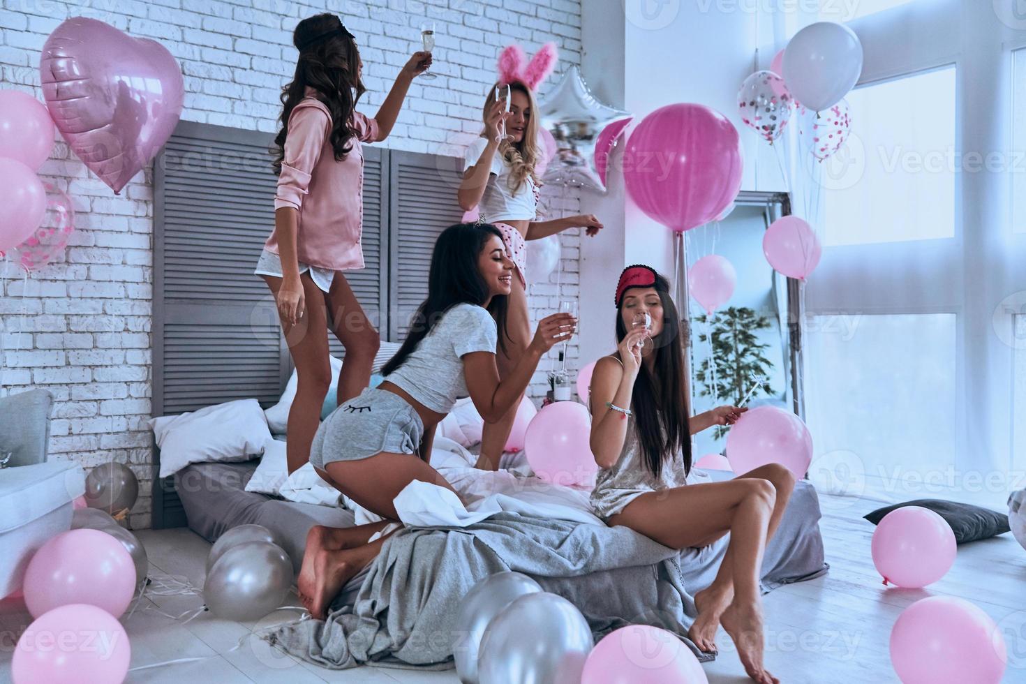 tempo de qualidade com os amigos. quatro jovens sorridentes brincalhões de pijama se unindo enquanto fazem uma festa do pijama no quarto com balões por todo o lugar foto