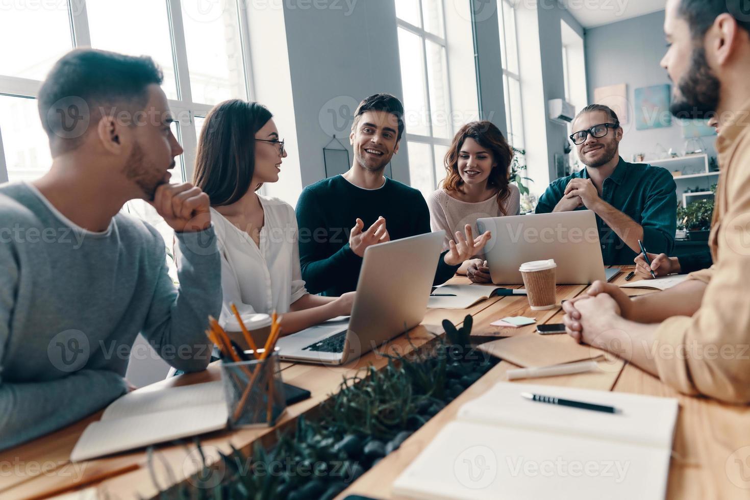 confiante e inteligente. grupo de jovens modernos em roupas casuais inteligentes discutindo algo e sorrindo enquanto trabalhava no escritório criativo foto