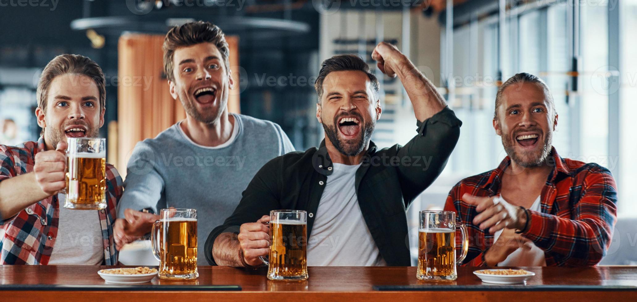 torcendo por jovens em roupas casuais bebendo cerveja e assistindo jogo esportivo foto