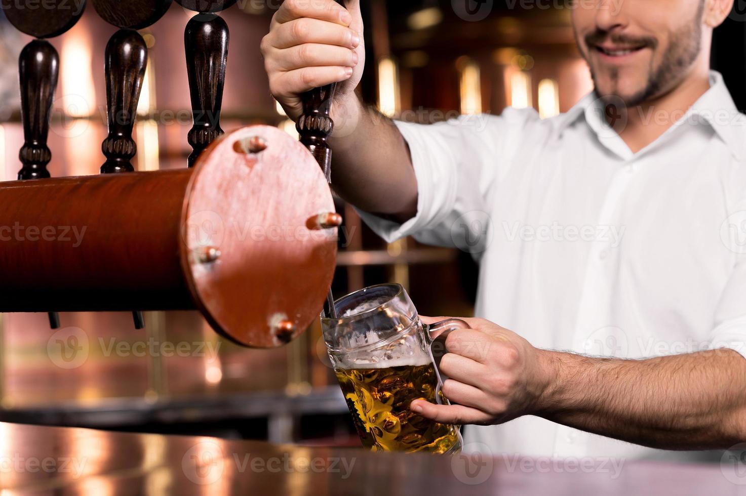 derramando cerveja. imagem recortada de barman sorridente servindo cerveja para a caneca foto