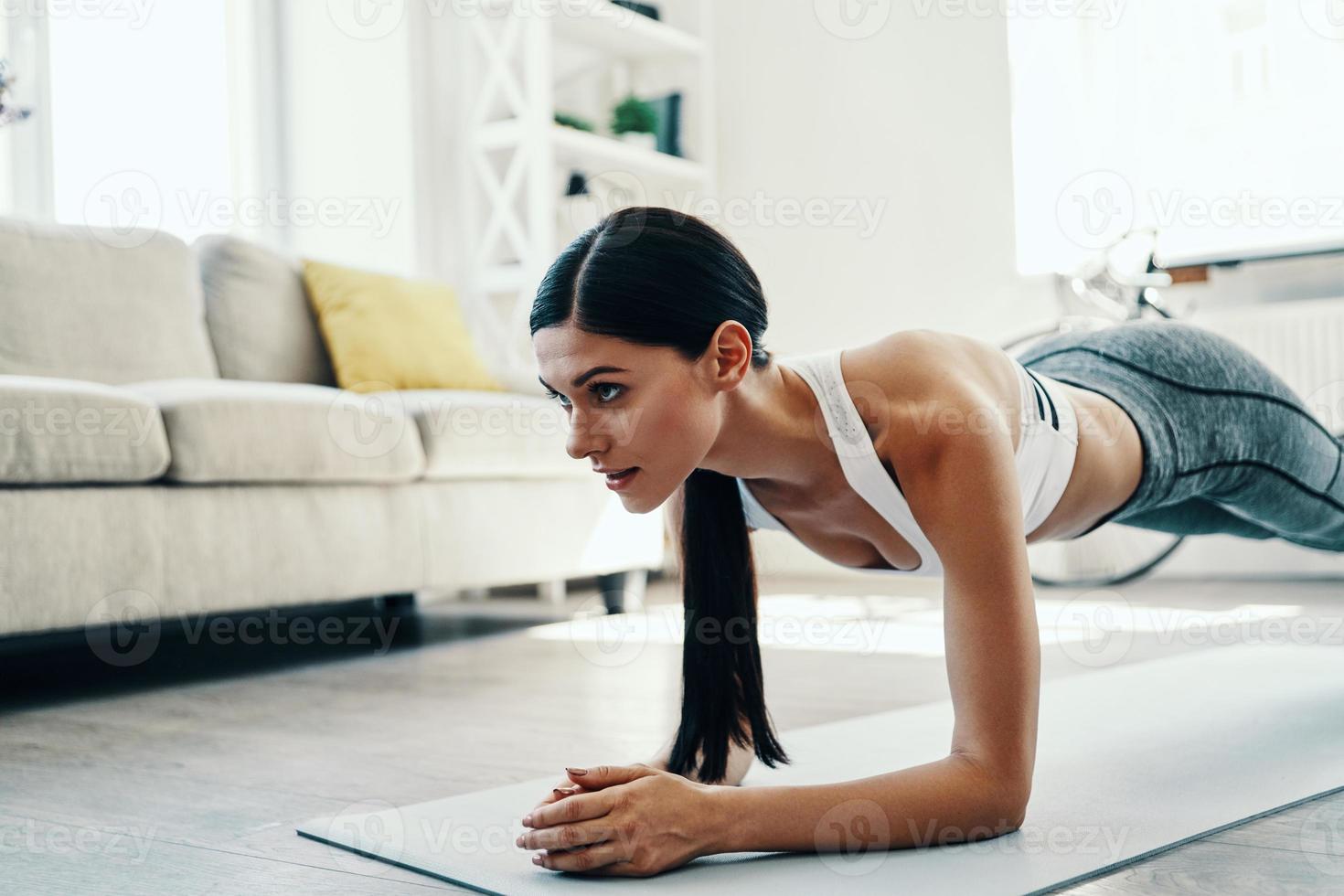 você pode fazê-lo linda jovem em roupas esportivas, mantendo a posição de prancha enquanto passa o tempo em casa foto