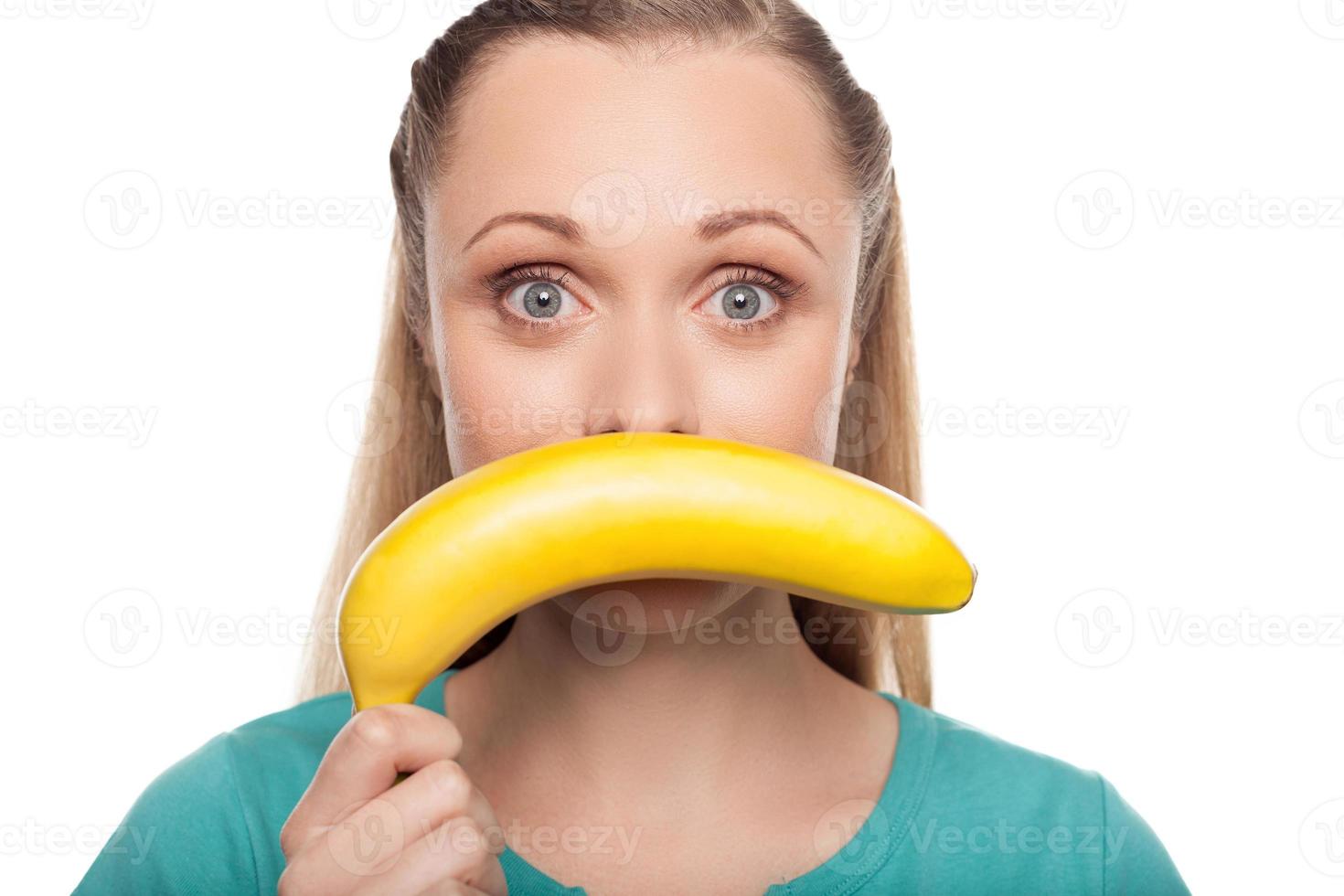 mulher com banana. bela jovem segurando banana na frente do rosto e expressando positividade enquanto isolado no branco foto