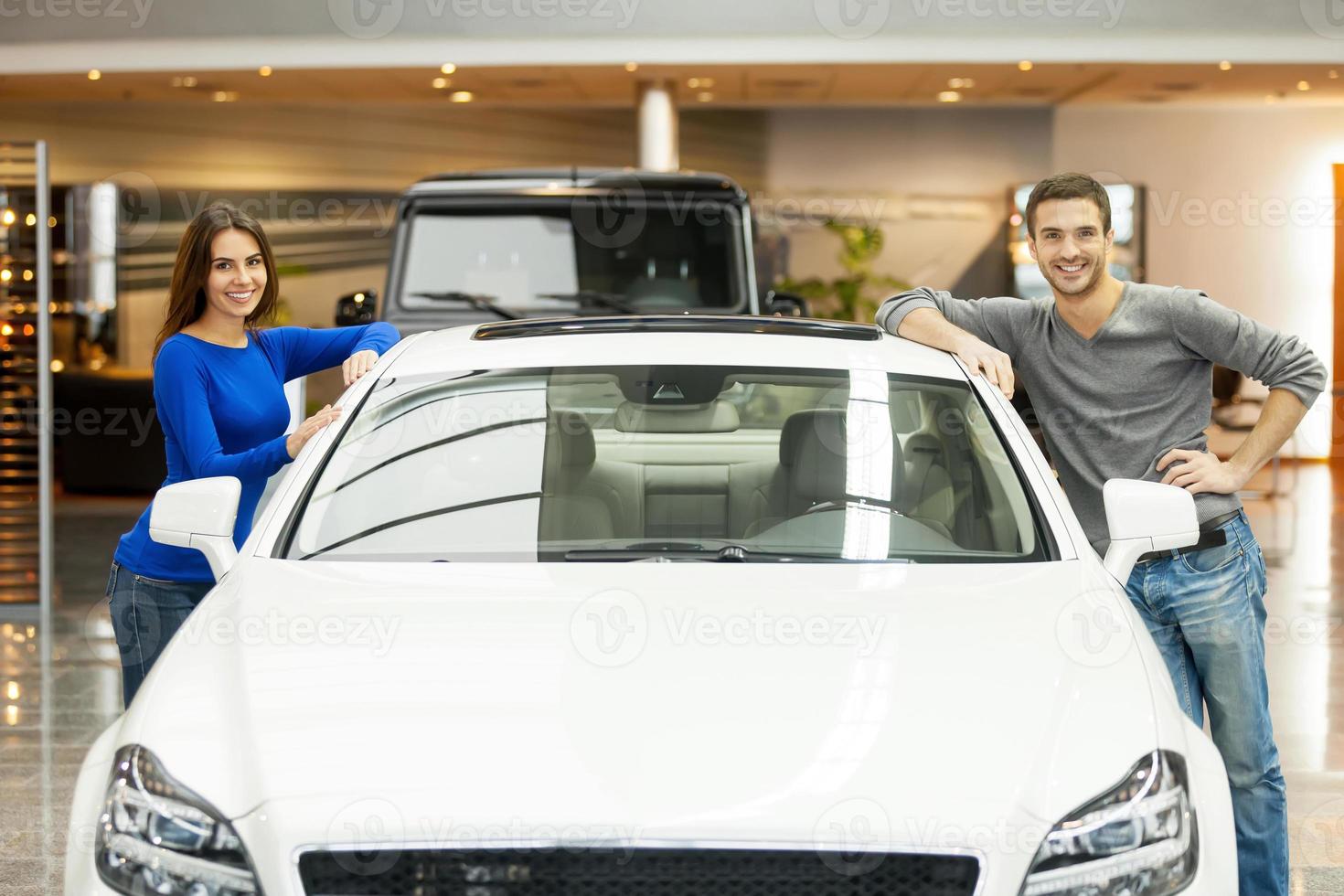 feliz com seu novo carro. casal jovem feliz dançando em ambos os lados do carro sorrindo para a câmera foto