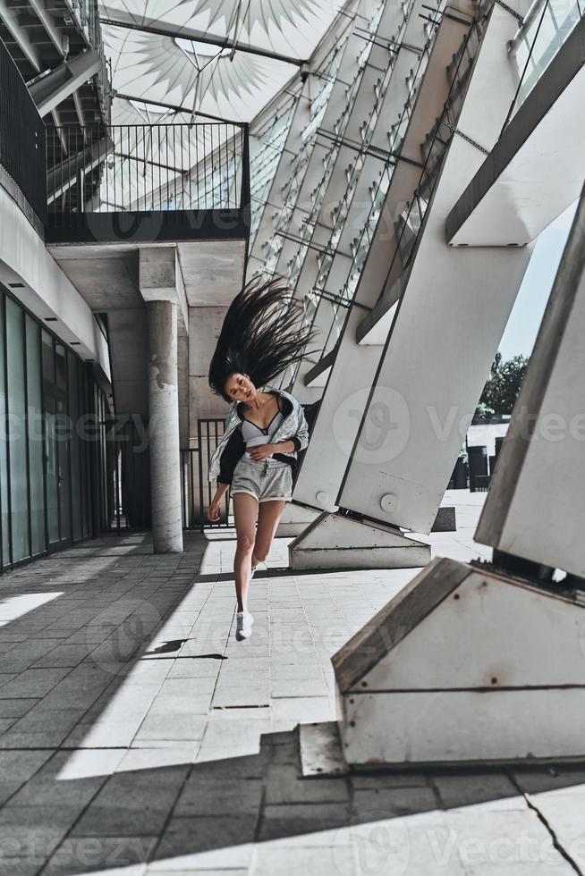 desafiando a si mesma. comprimento total de mulher jovem e atraente em roupas casuais, olhando para a câmera enquanto corre ao ar livre foto