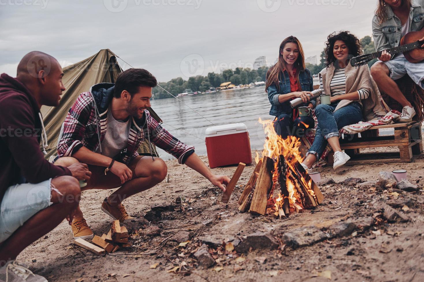 tempo despreocupado com os amigos. grupo de jovens em roupas casuais sorrindo enquanto desfruta de festa na praia perto da fogueira foto