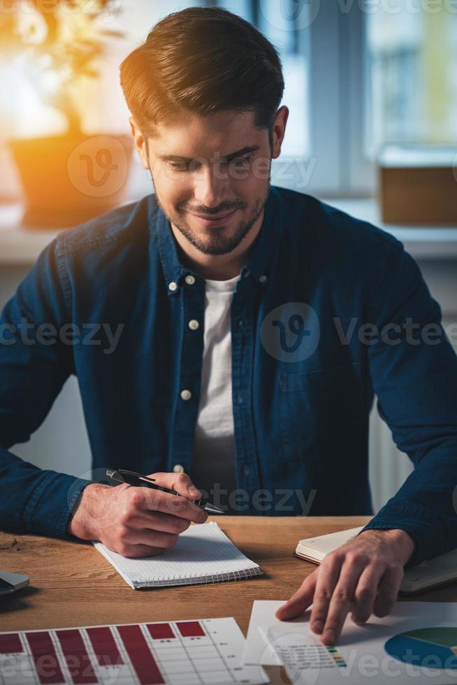 eu posso ver o crescimento aqui alegre jovem bonito trabalhando com gráficos com sorriso enquanto está sentado em seu local de trabalho foto