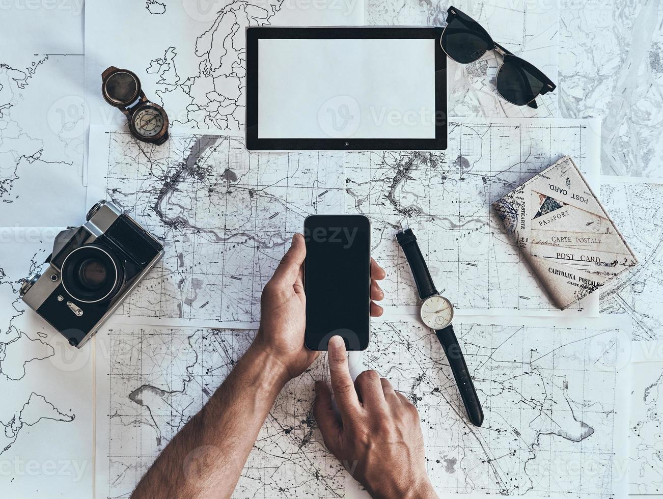 continue viajando. close-up vista superior do homem usando telefone inteligente com óculos de sol, câmera fotográfica, bússola, relógio e passaporte deitado no mapa ao redor foto