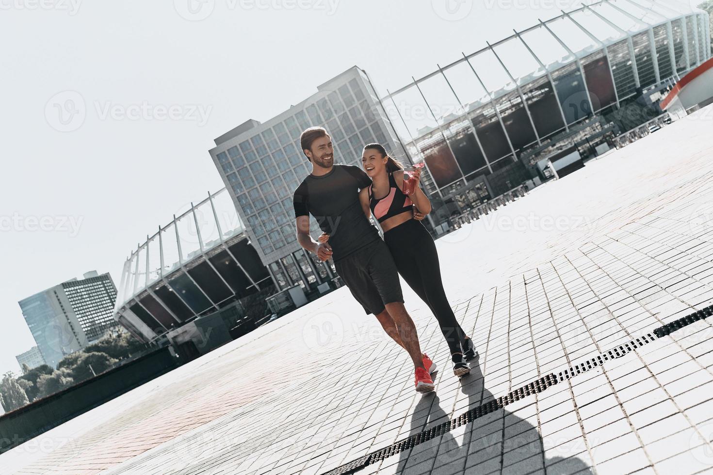 feliz após o treino. comprimento total do jovem casal em roupas esportivas, unindo-se e sorrindo enquanto caminhava ao ar livre foto