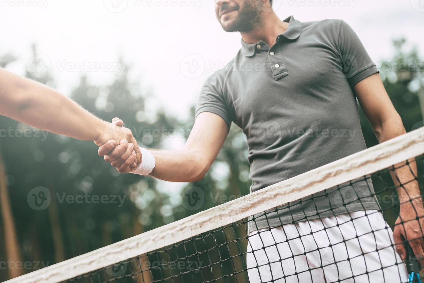 obrigado pela imagem conceitual de visão de baixo ângulo do jogo de dois homens em roupas esportivas apertando as mãos em pé perto da rede de tênis na quadra foto