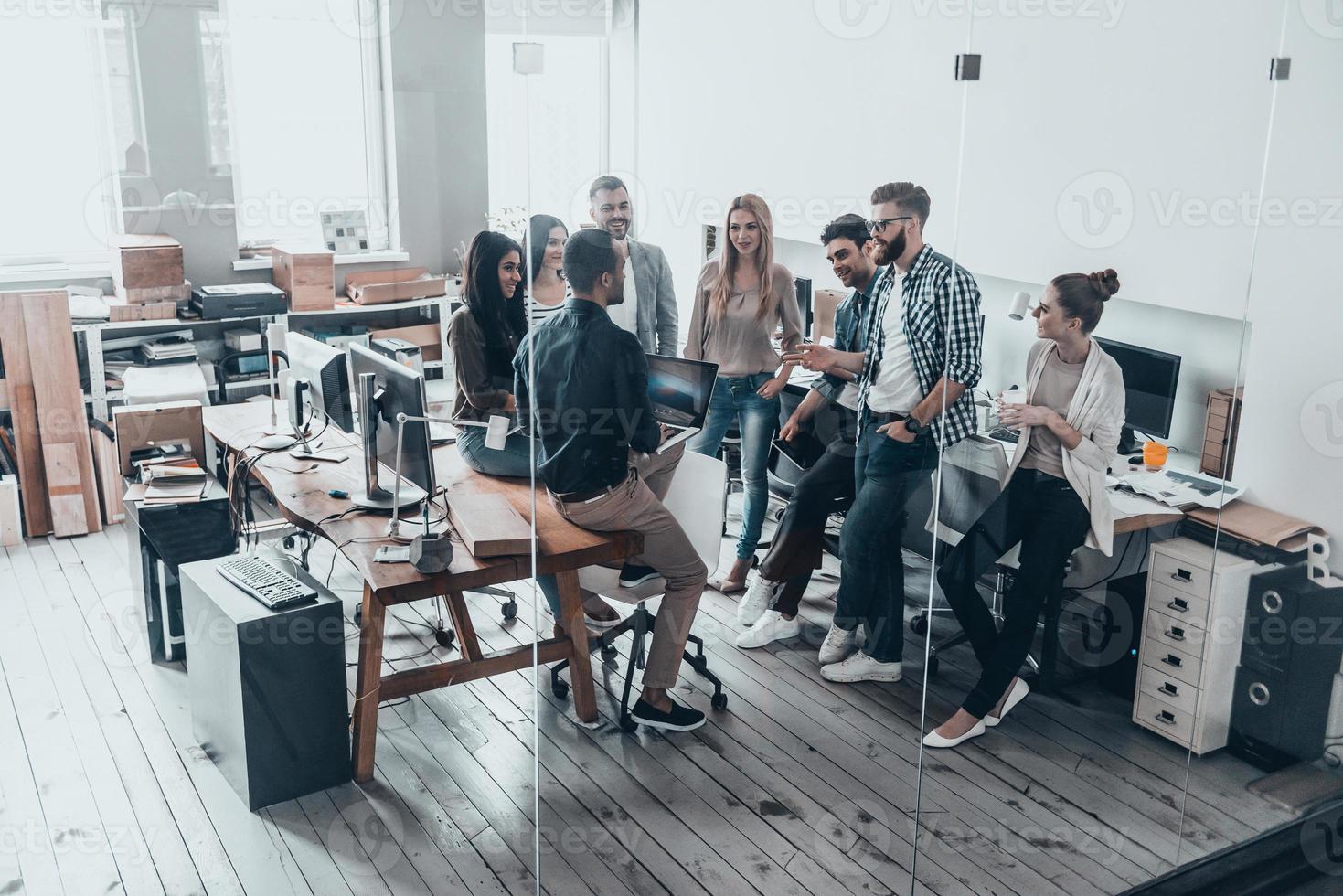 equipe de inovadores. vista superior de corpo inteiro de jovens modernos em roupas casuais inteligentes falando e sorrindo em pé atrás da parede de vidro no escritório criativo foto