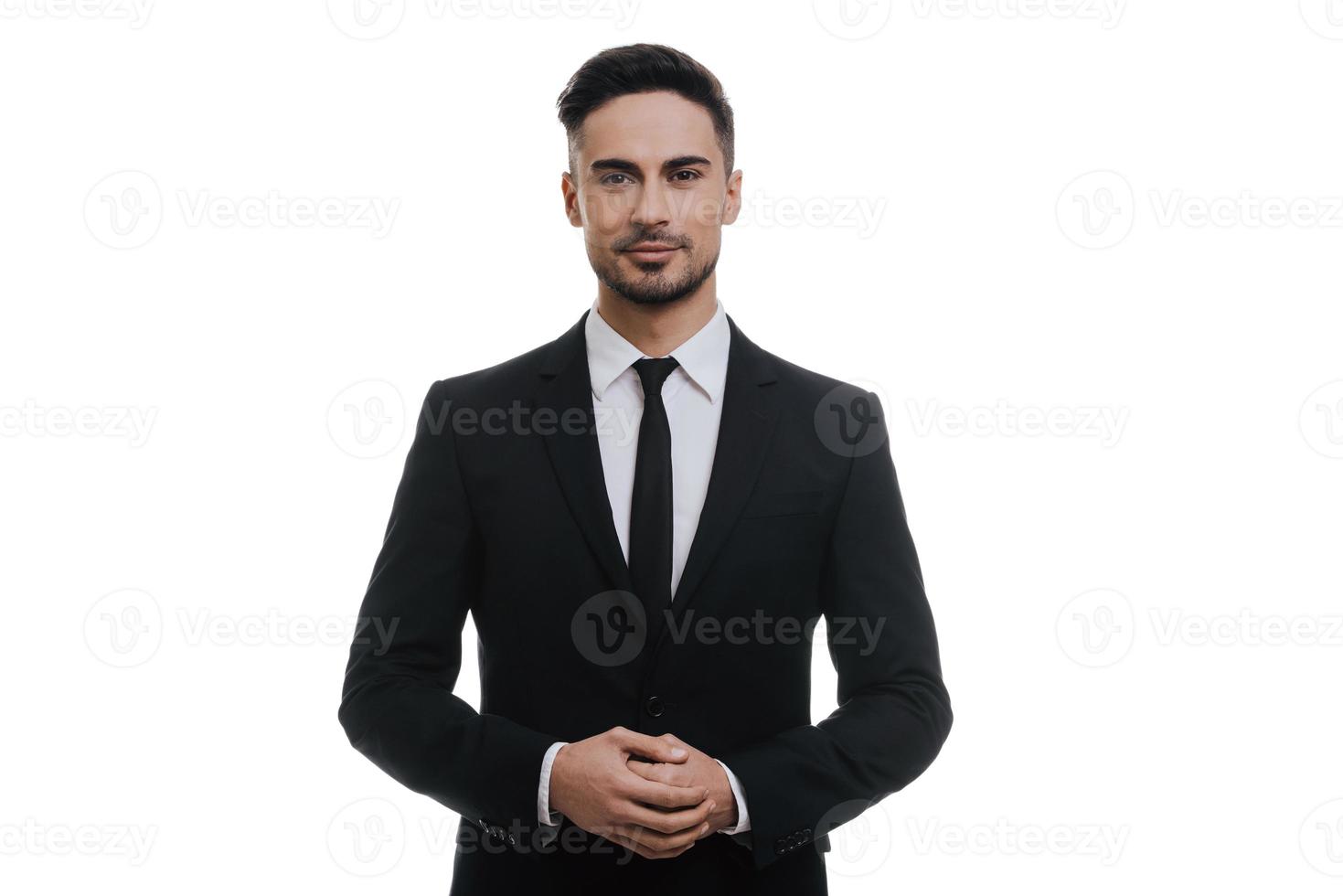 confiança e carisma. jovem bonito de terno completo, de mãos dadas e olhando para a câmera em pé contra um fundo branco foto