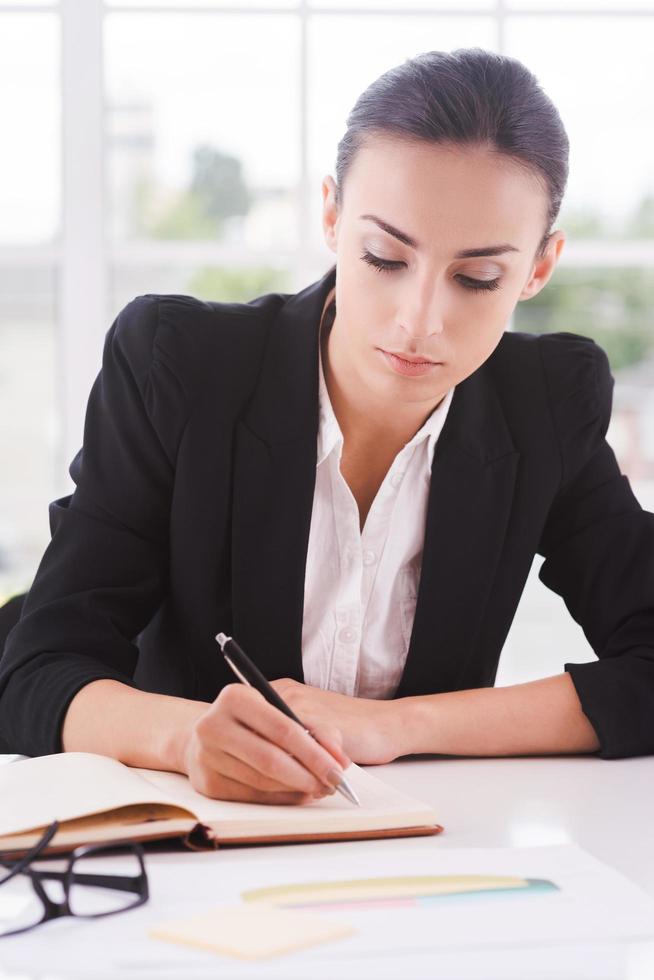 empresária no trabalho. negócios jovem confiante escrevendo algo no papel enquanto está sentado em seu local de trabalho foto