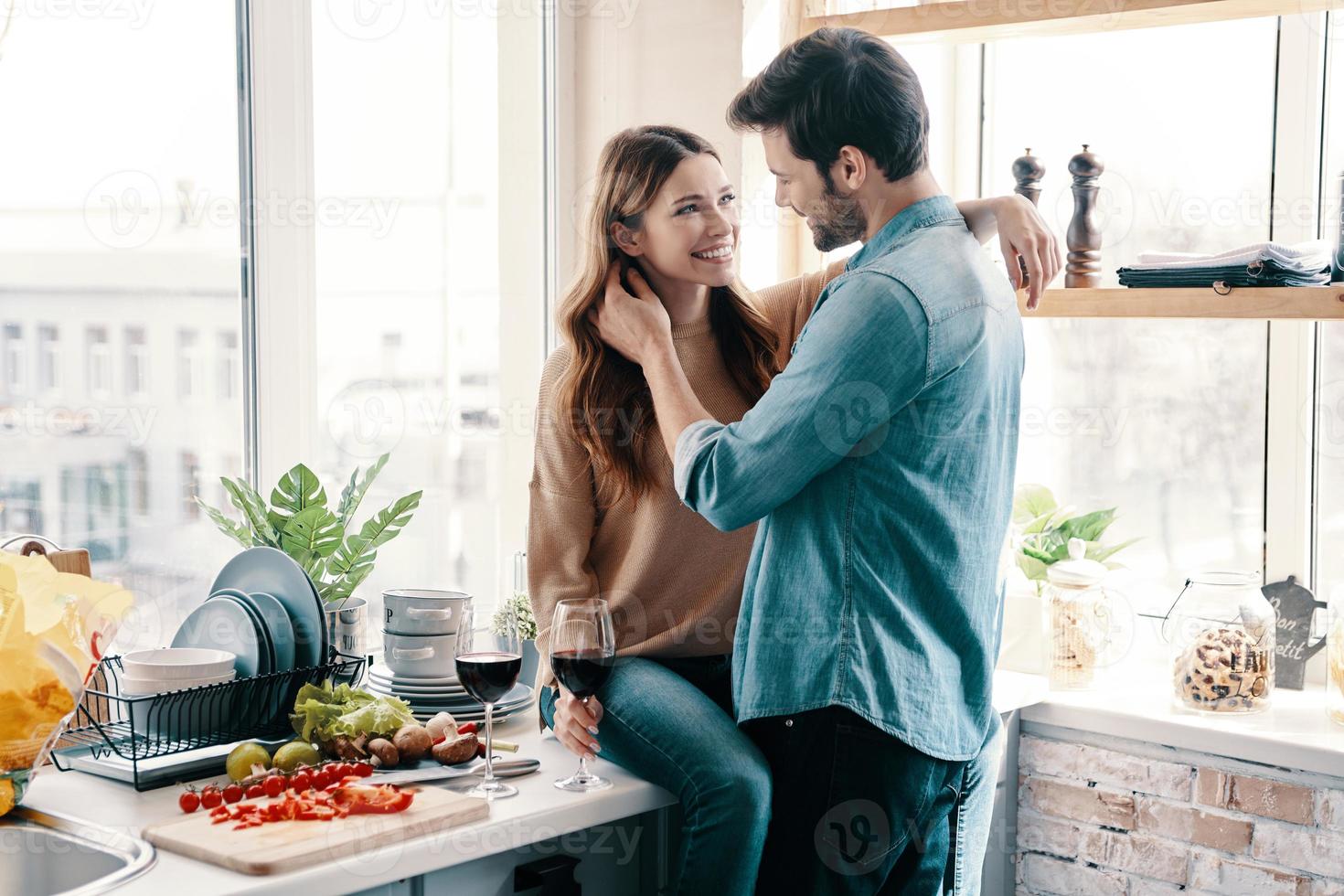 amando tudo nela. lindo casal jovem cozinhando o jantar e bebendo vinho em pé na cozinha em casa foto