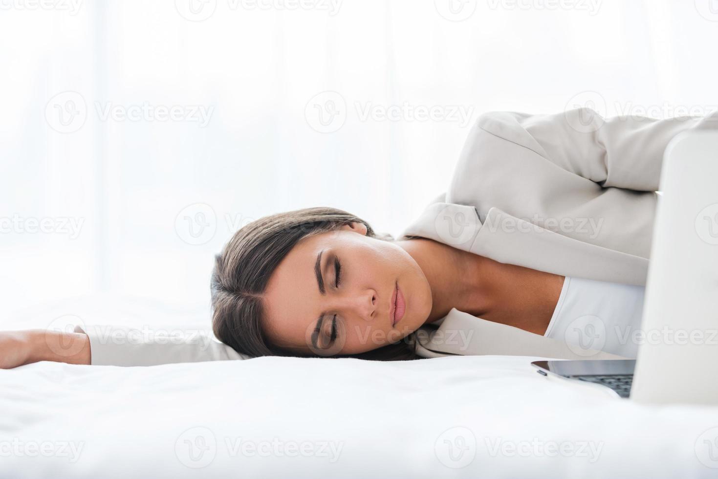 empresária cansada. bela jovem empresária de terno dormindo deitada na cama foto