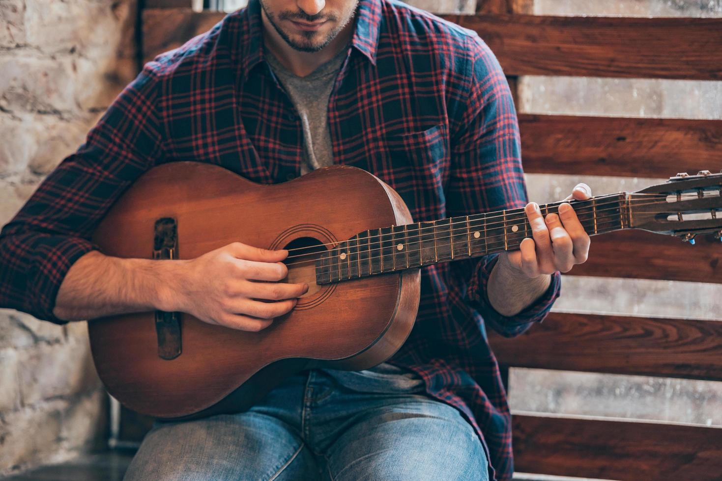 tocando riffs perfeitos. parte de close-up do jovem tocando violão enquanto está sentado no parapeito da janela foto